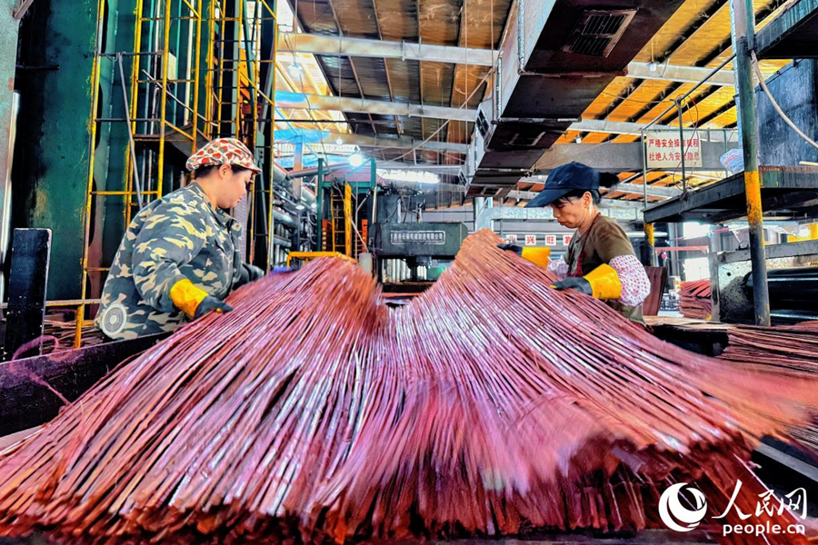 員工將竹簾與木板逐層鋪展在熱壓機下。人民網(wǎng) 李唯一攝