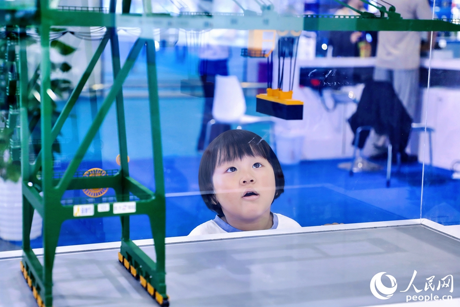 小朋友端詳岸邊集裝箱起重機設(shè)備模型。人民網(wǎng) 李唯一攝