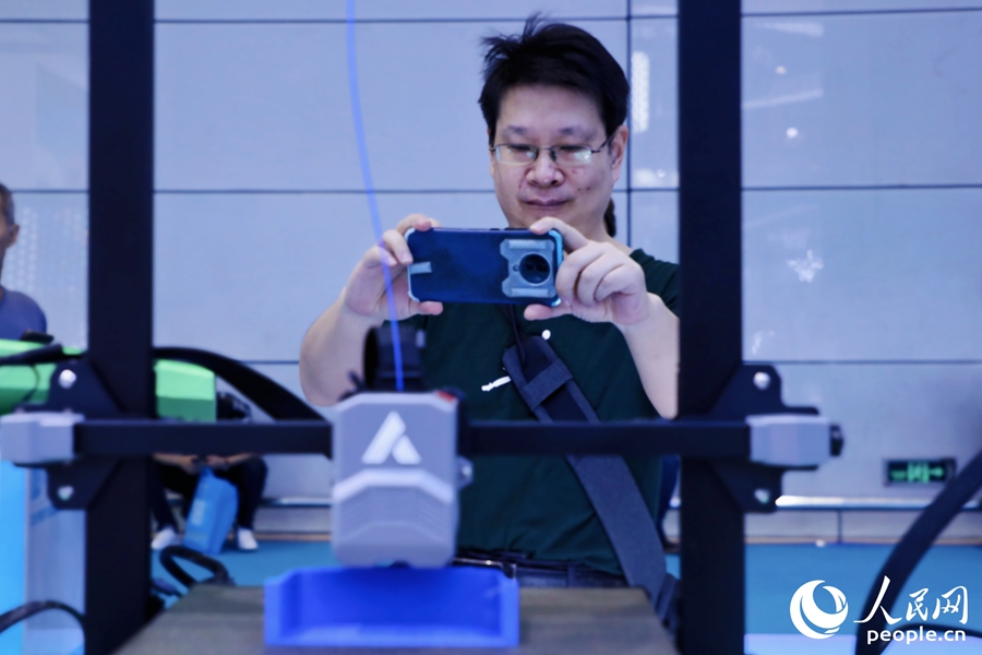 觀眾饒有興趣地用手機拍攝正在運行的3D打印設(shè)備。人民網(wǎng) 李唯一攝